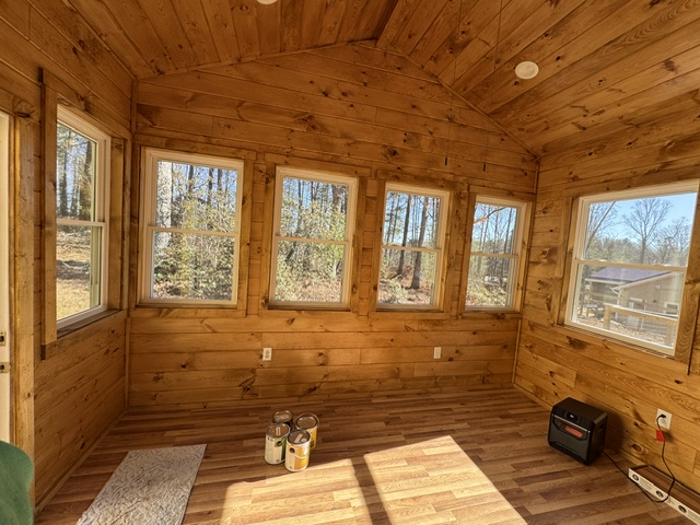 Vaulted interior sunroom addition with tongue-and-groove pine wood plank walls, recessed pot lighting, wood laminate flooring, and panoramic window layout