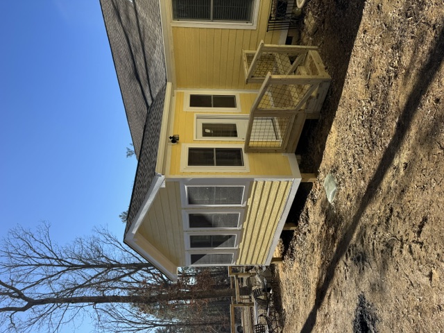 Custom home sunroom addition exterior with architectural shingle roof, matching yellow lap siding, multi-window wall, and custom wood landing stair