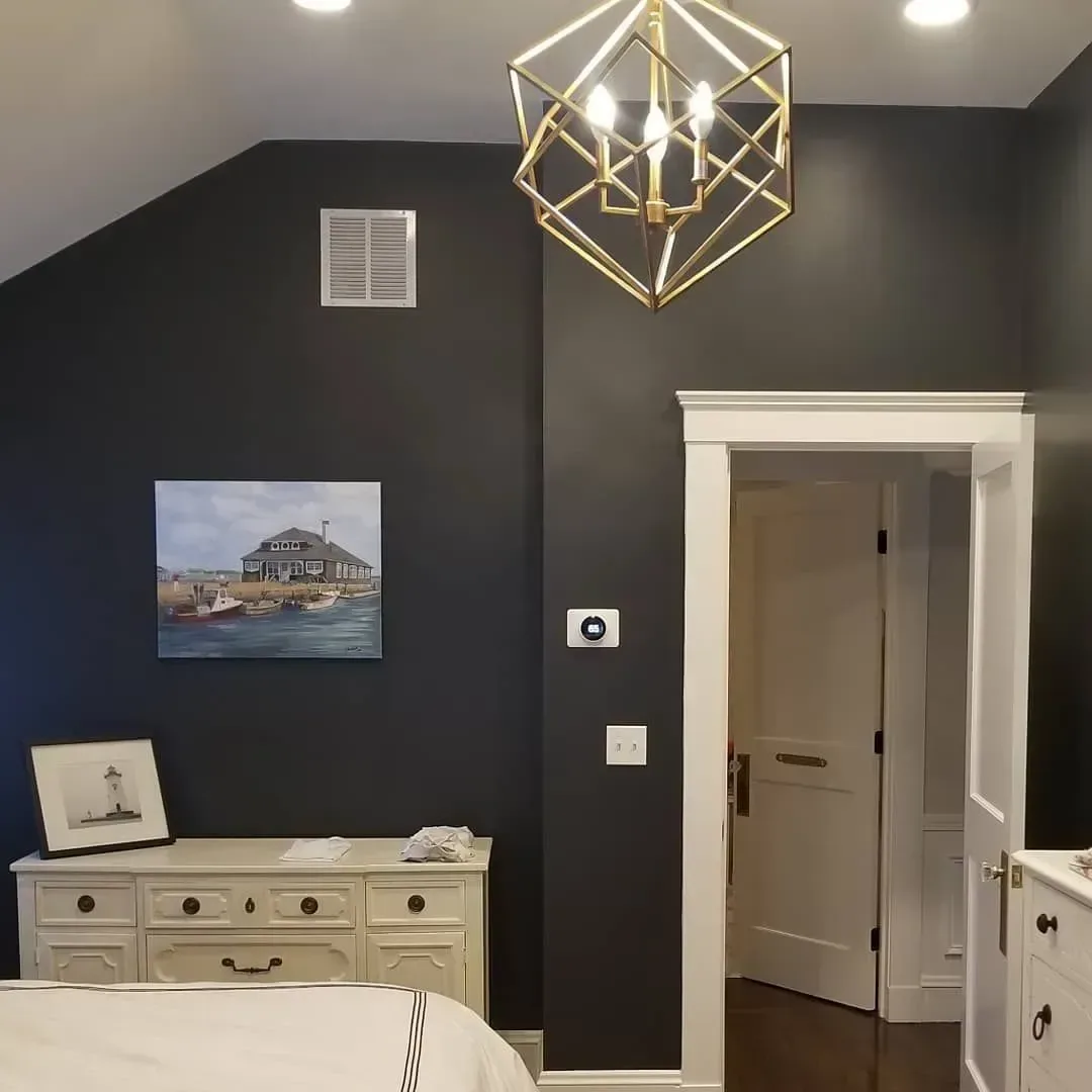 Dark gray bedroom with white trim, dresser, and doorway. Gold geometric light fixture hangs from ceiling.