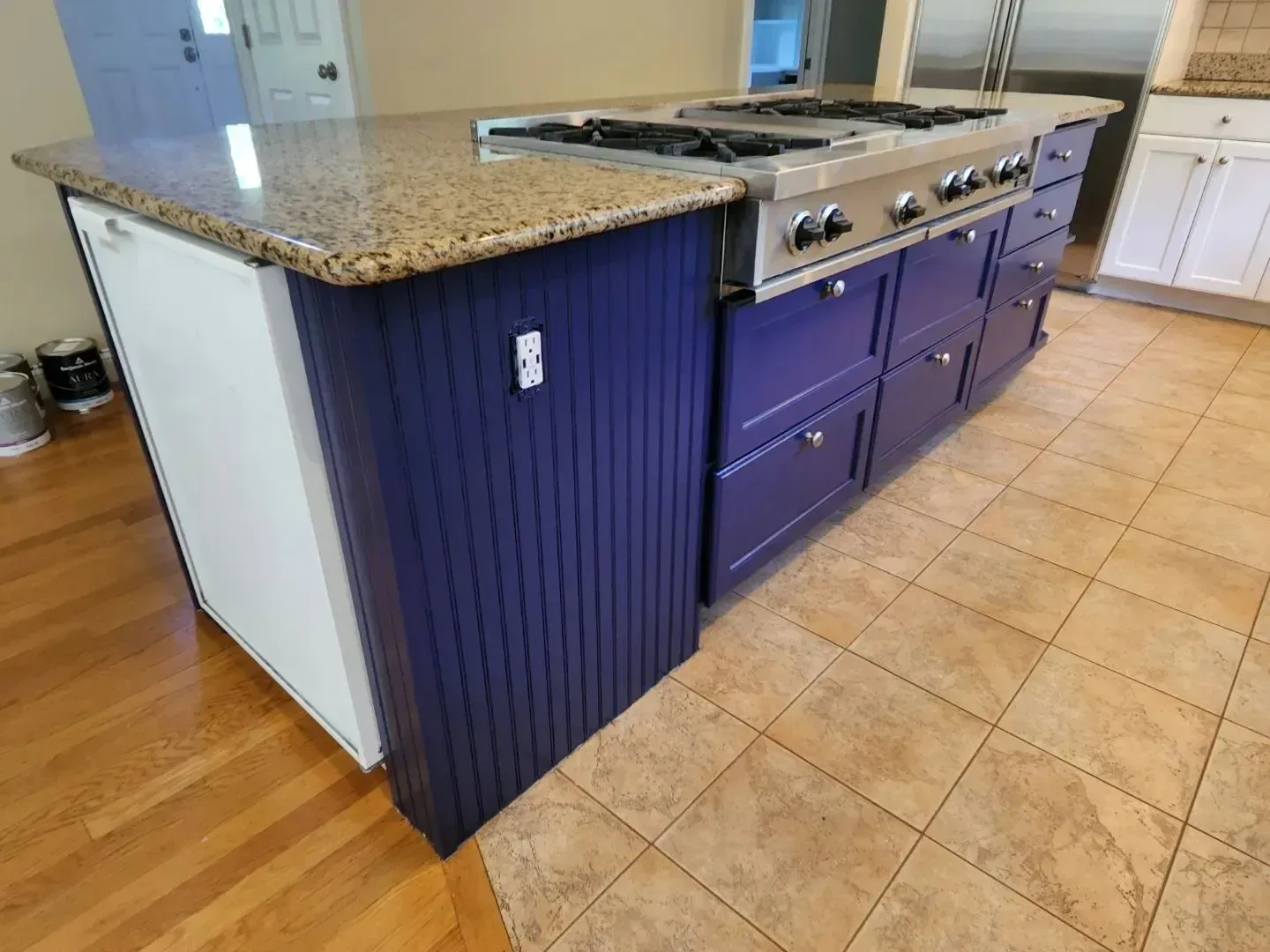 Kitchen island with granite countertop, blue cabinets, gas range, and dishwasher.