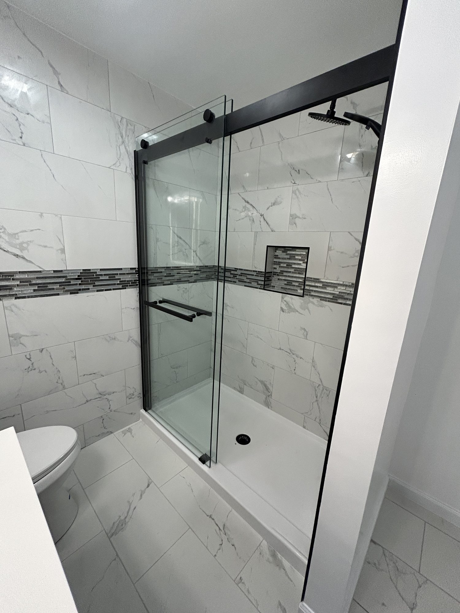 Walk-in shower with marbled porcelain tile, glass mosaic band, niche, and black sliding glass door, Reno, NV