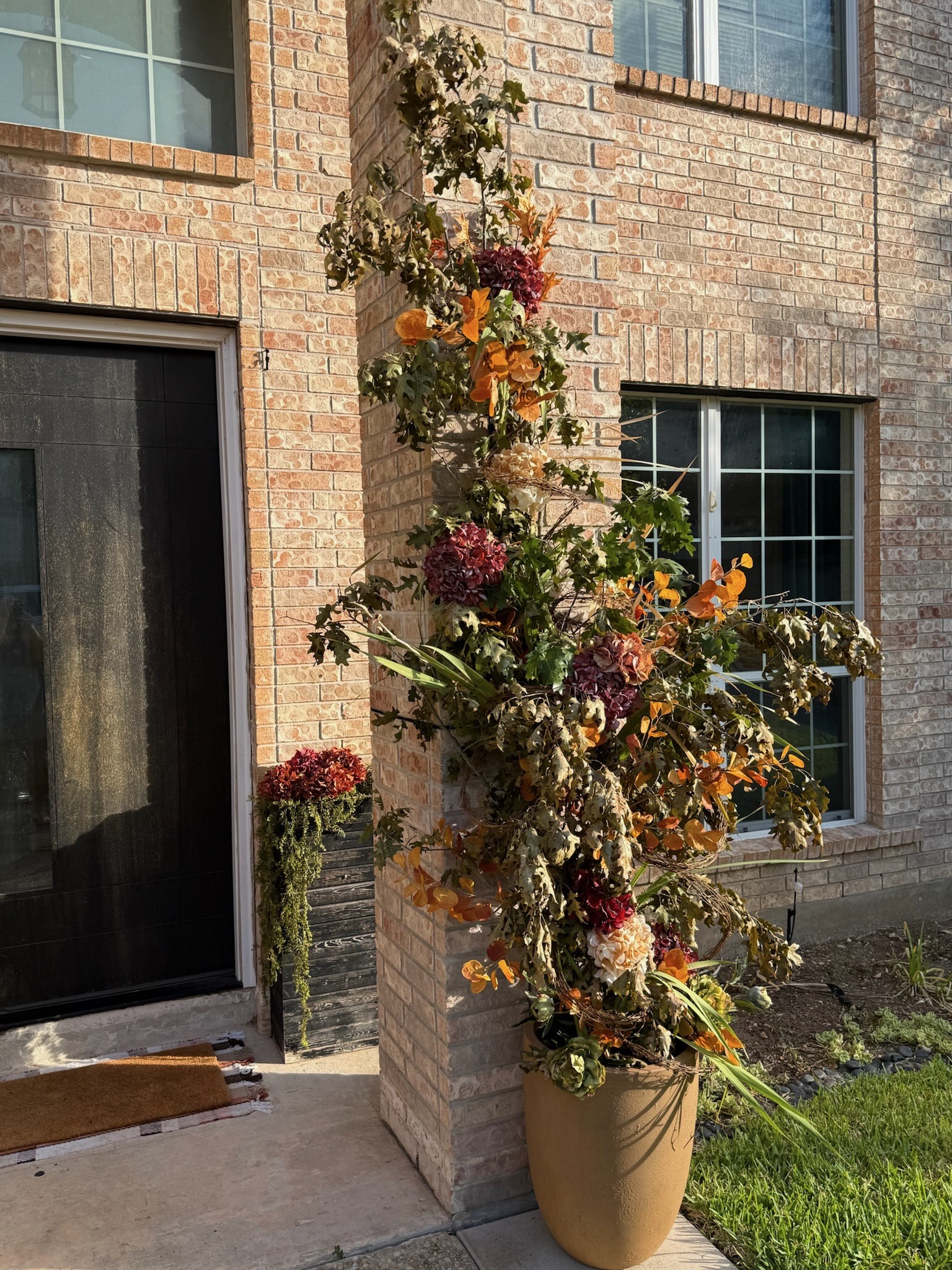 Close-up of artisan floral column installation climbing a San Antonio brick pillar with rich autumn florals, dried hydrangeas, and greenery