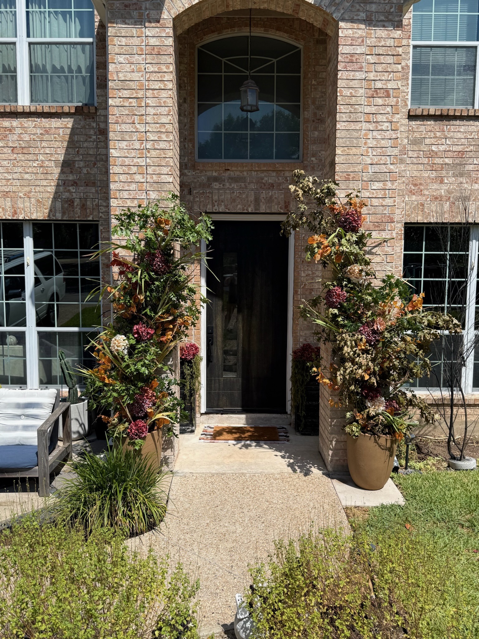 Two-story brick entryway with tall custom floral urn arrangements and arched dried floral installations framing the doorway in San Antonio
