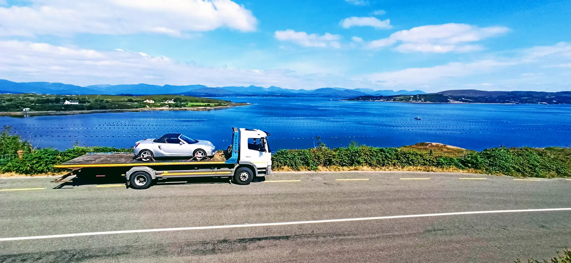NO1 RECOVERY tow truck carrying car along scenic Irish road