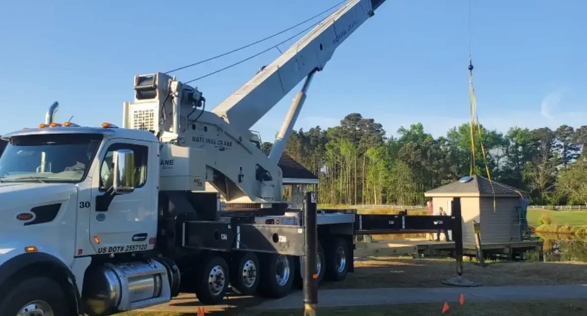 Crane-assisted tree removal lifting a tree section over a home