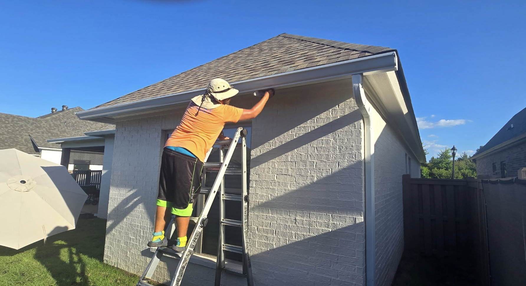 Kayne cleaning gutters and inspecting downspouts on residential brick home