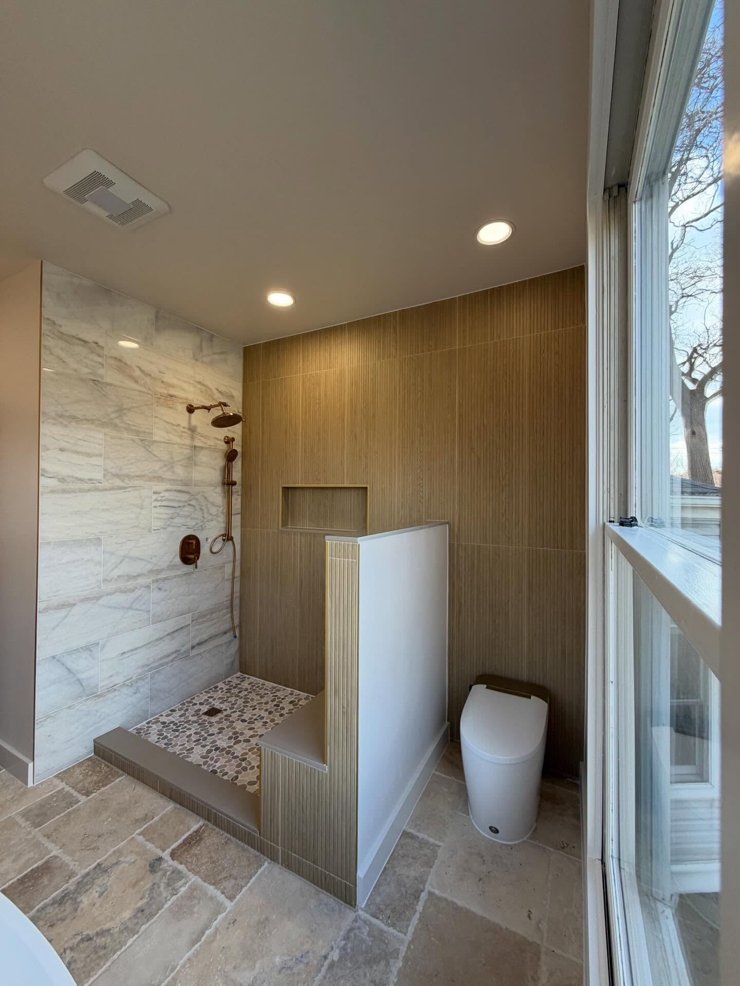Walk-in shower with warm wood-look vertical wall tile, marble-look shower tile, built-in niche, and partial-height partition wall.