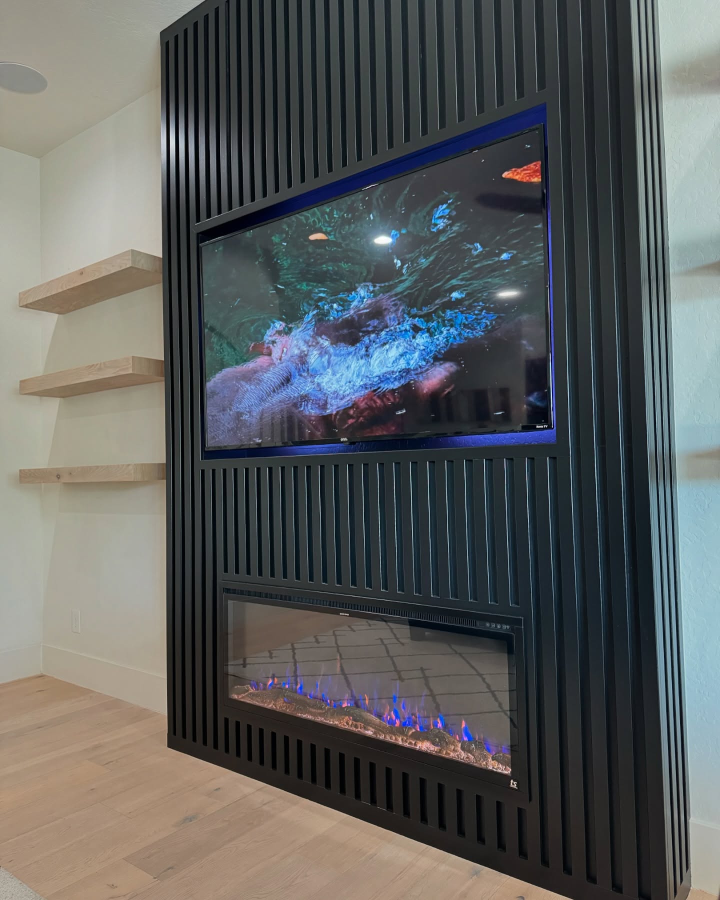 Detail view of the custom black slat feature wall with recessed TV niche and multicolor electric fireplace.