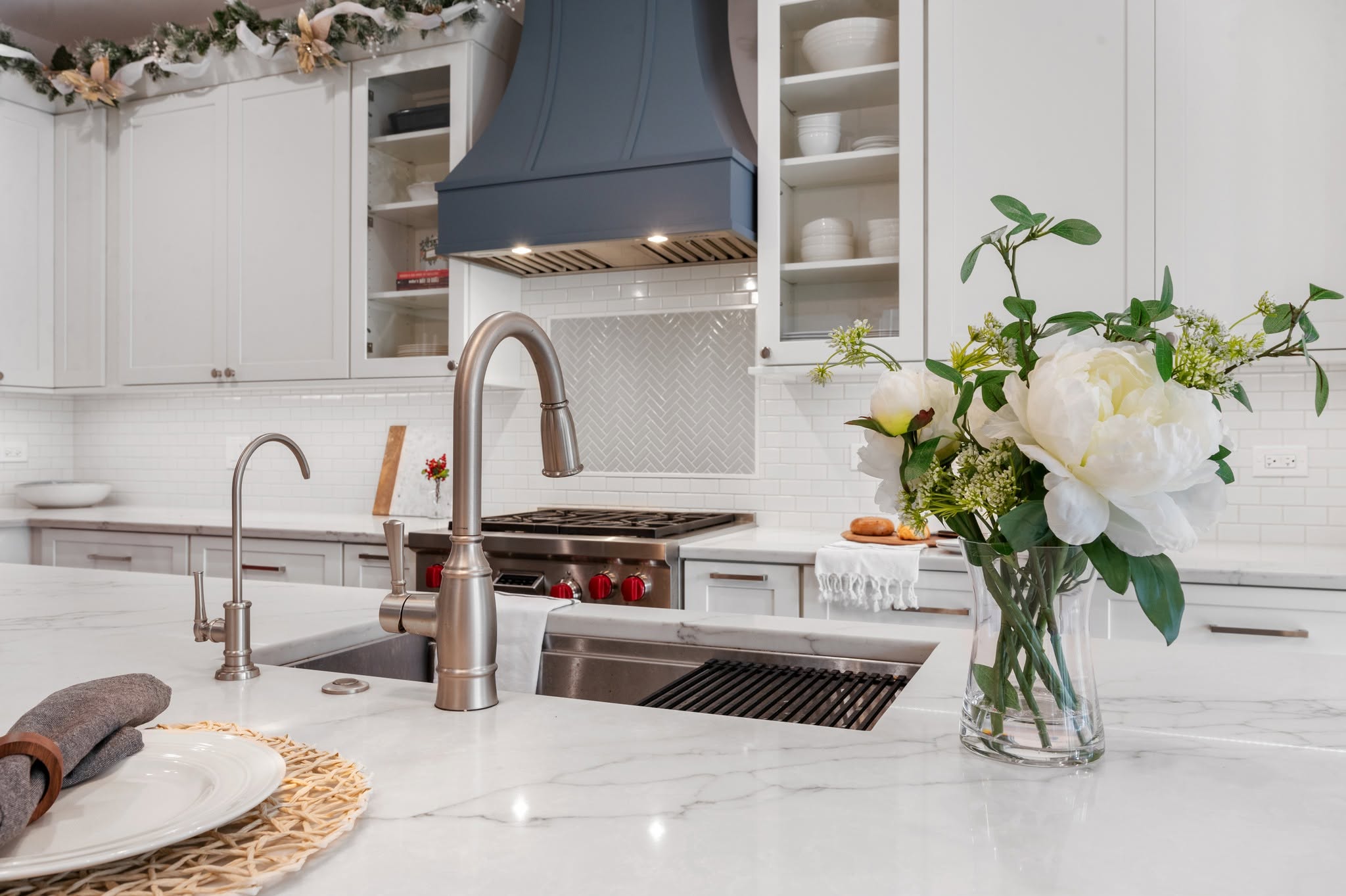 Close-up perspective of the quartz island countertop, stainless undermount sink, gooseneck pull-down faucet, and filtered water dispenser.