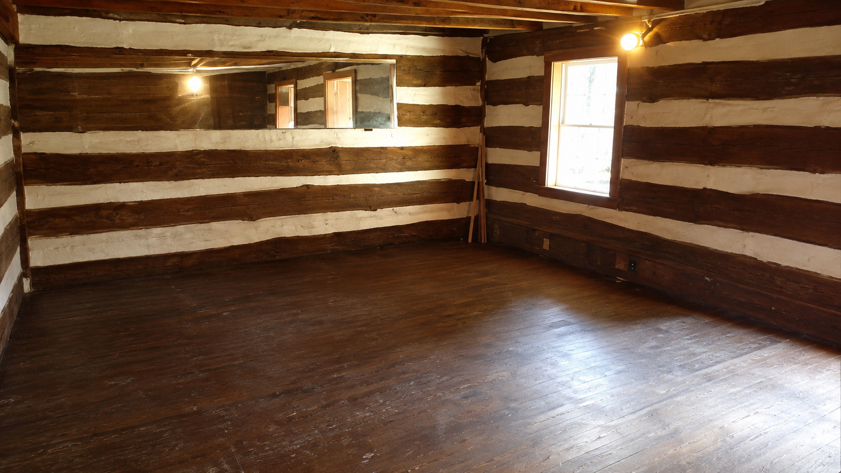 Spacious room with dark stained pine wood flooring, log beam walls, and warm lighting