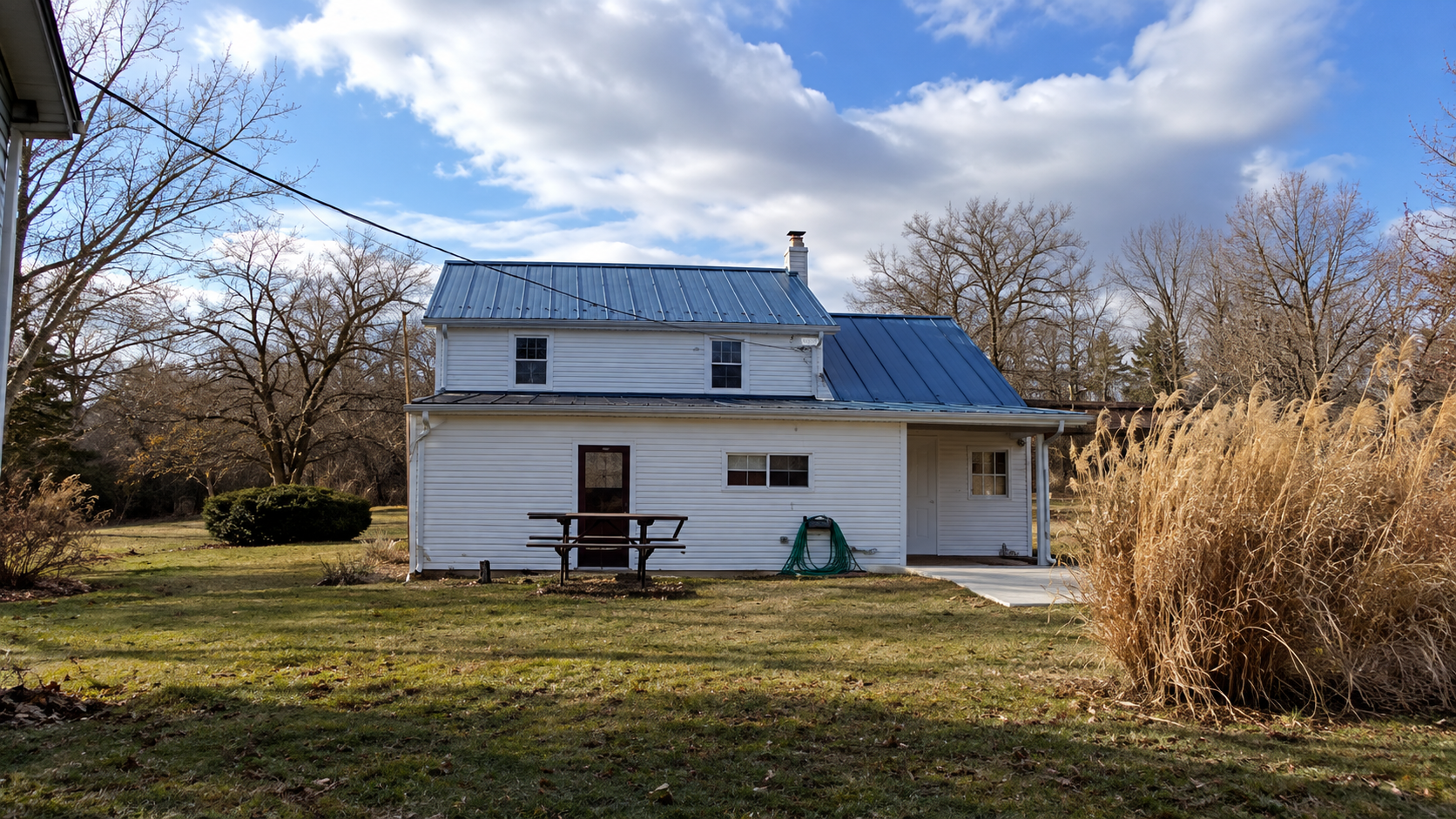 Rear yard view of the home showing lawn, picnic area, concrete patio, and mature trees