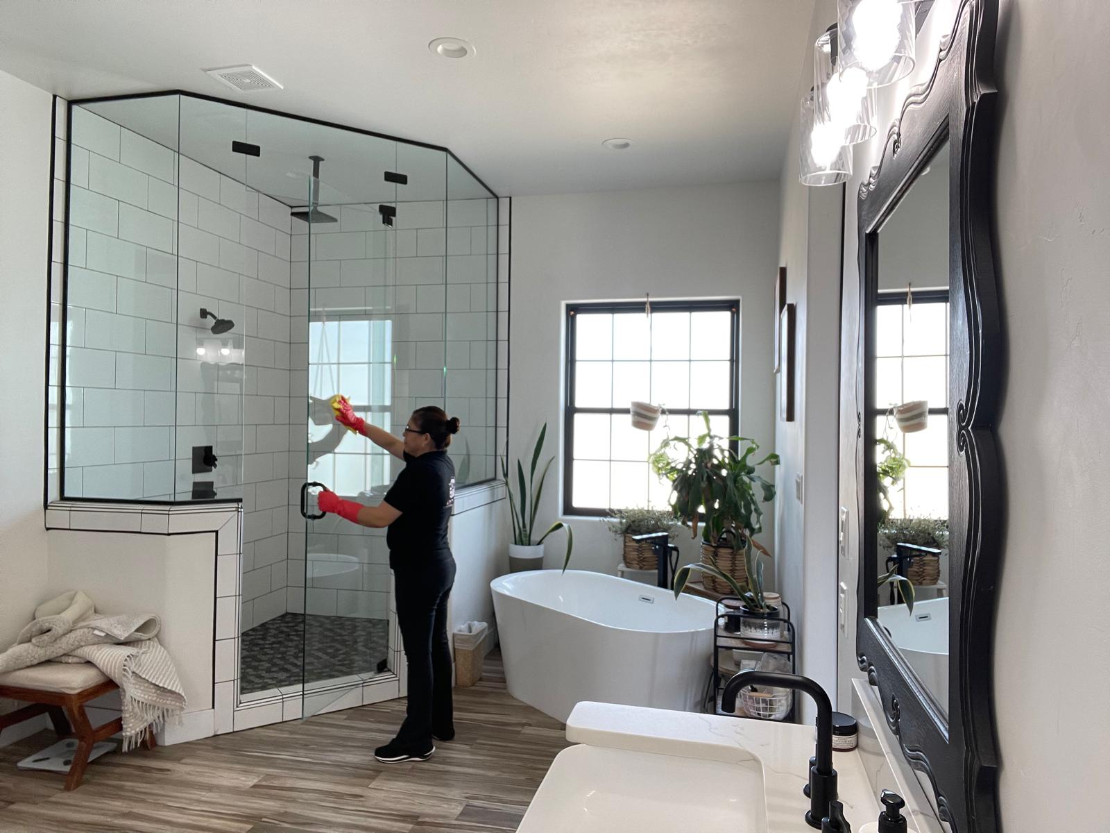 Adri's Cleaning Services specialist wiping down walk-in glass shower enclosure in Hobbs NM