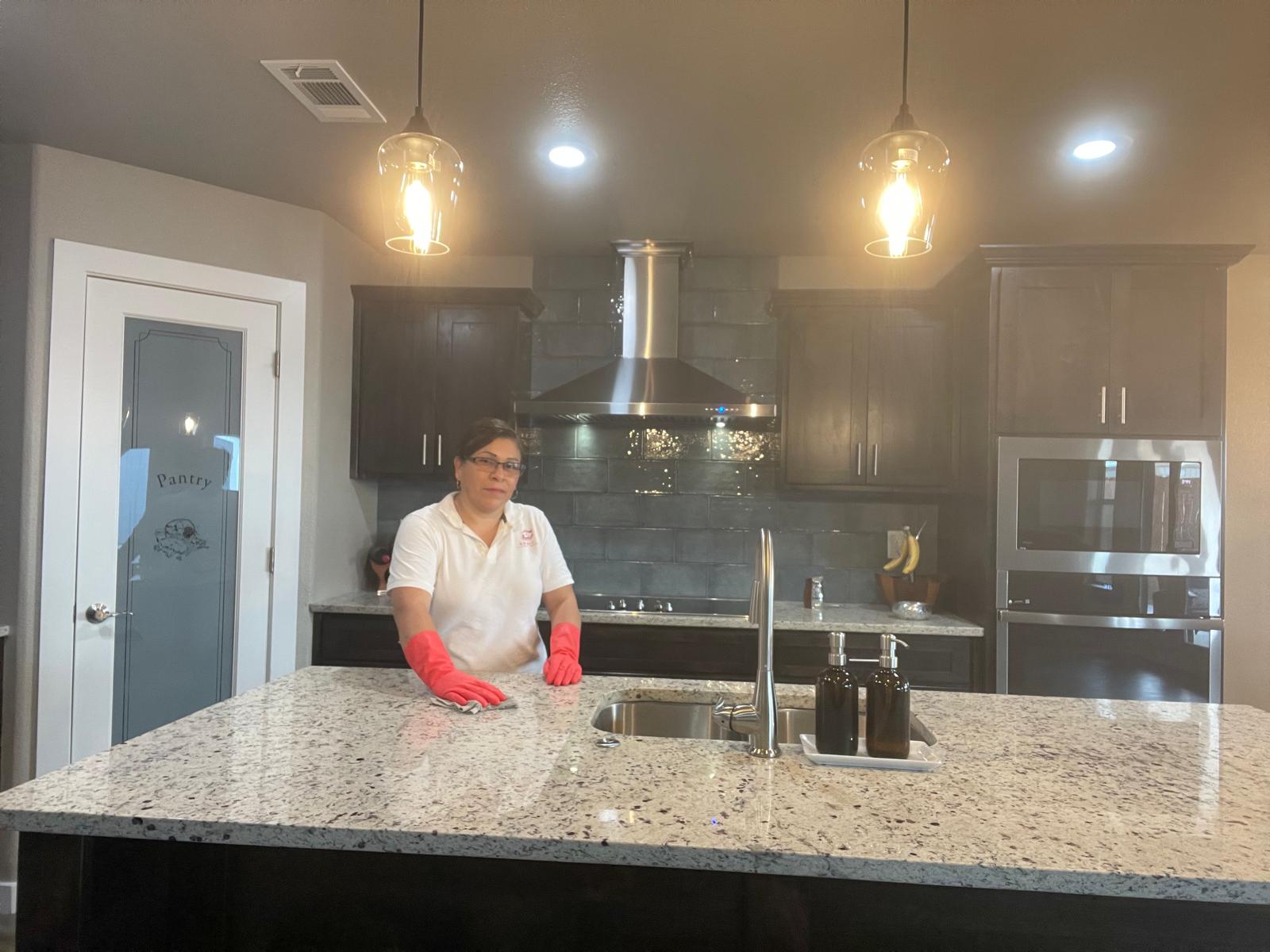 Adri's Cleaning Services professional sanitizing granite kitchen island with protective gloves in Hobbs NM