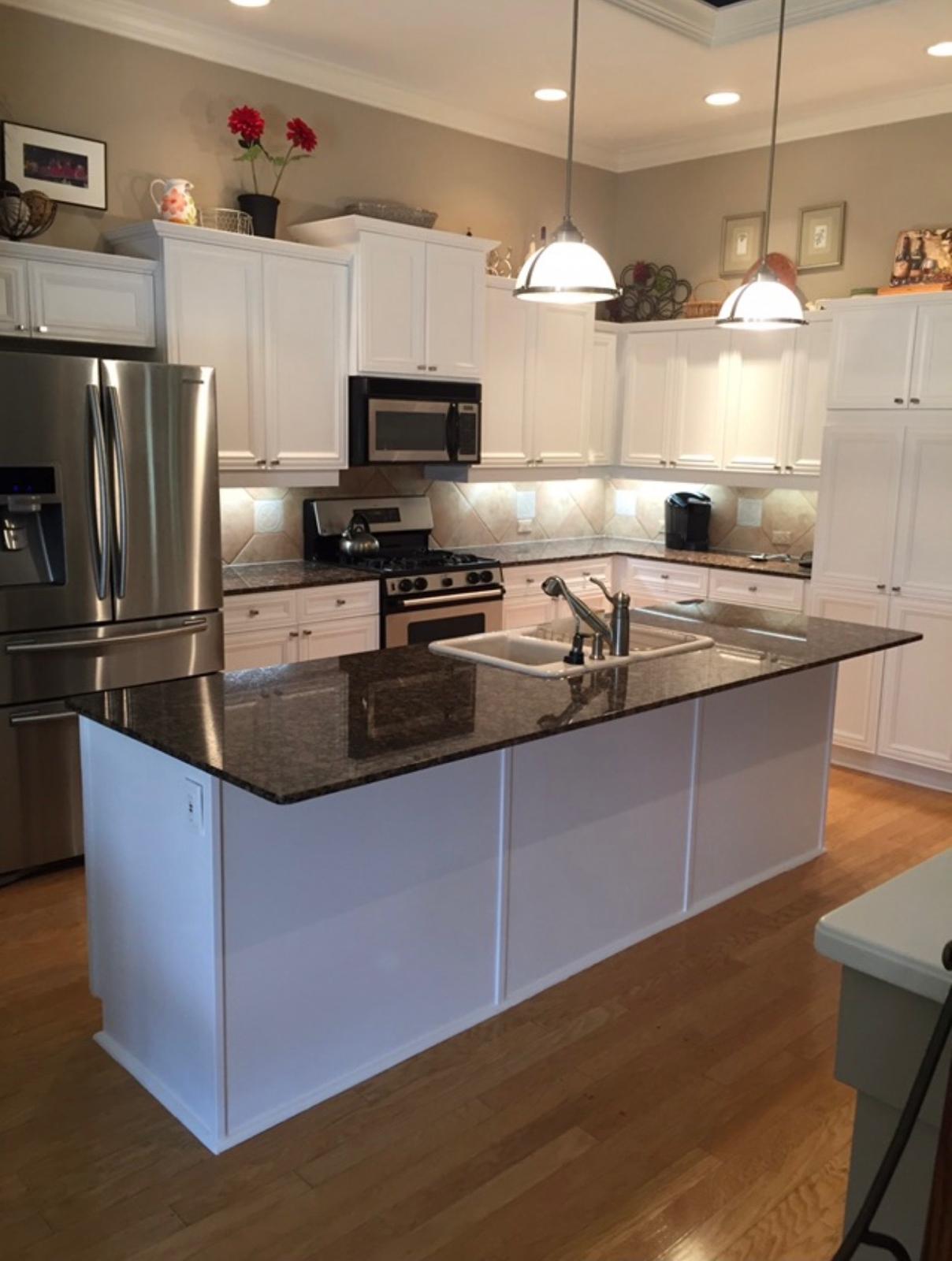 Completed kitchen cabinet spray painting in bright white finish with matching island and granite countertops in Wesley Chapel FL