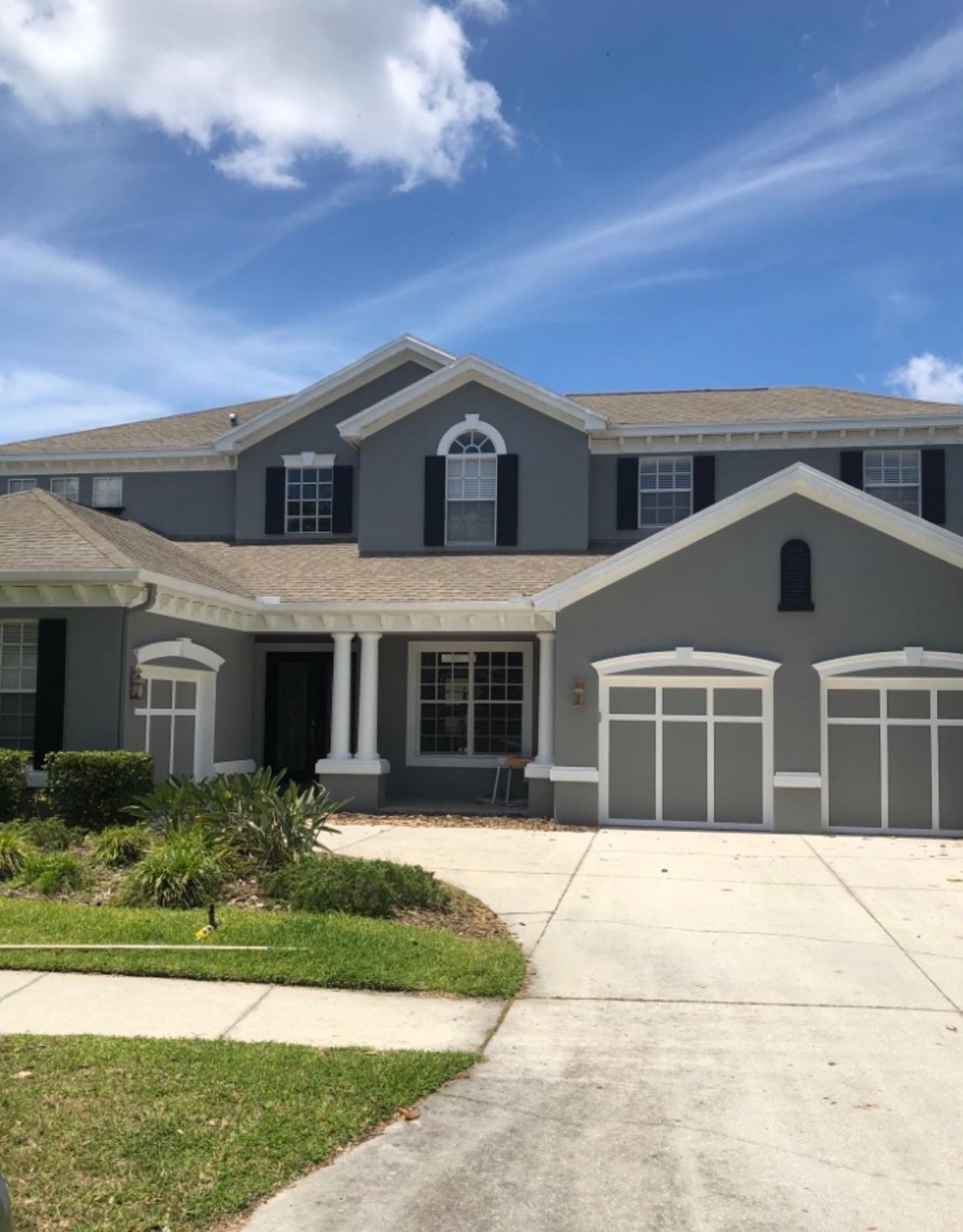 Completed exterior painting of grand two-story estate with modern slate grey stucco, crisp white columns, and matching carriage garage doors in Land O' Lakes FL