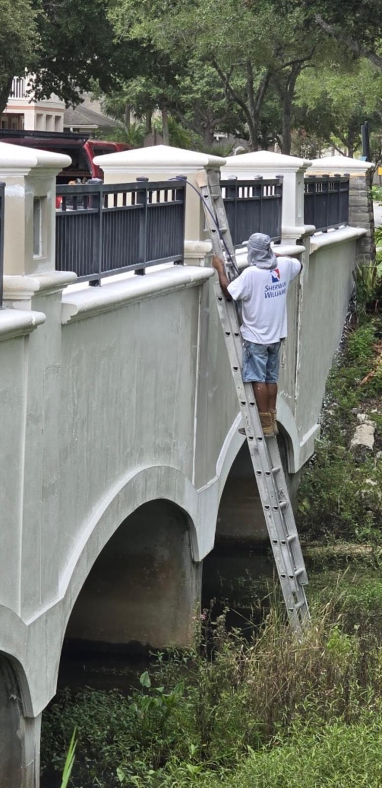 Ecuaconstruction craftsman using Sherwin-Williams coatings to paint exterior architectural bridge wall and parapet