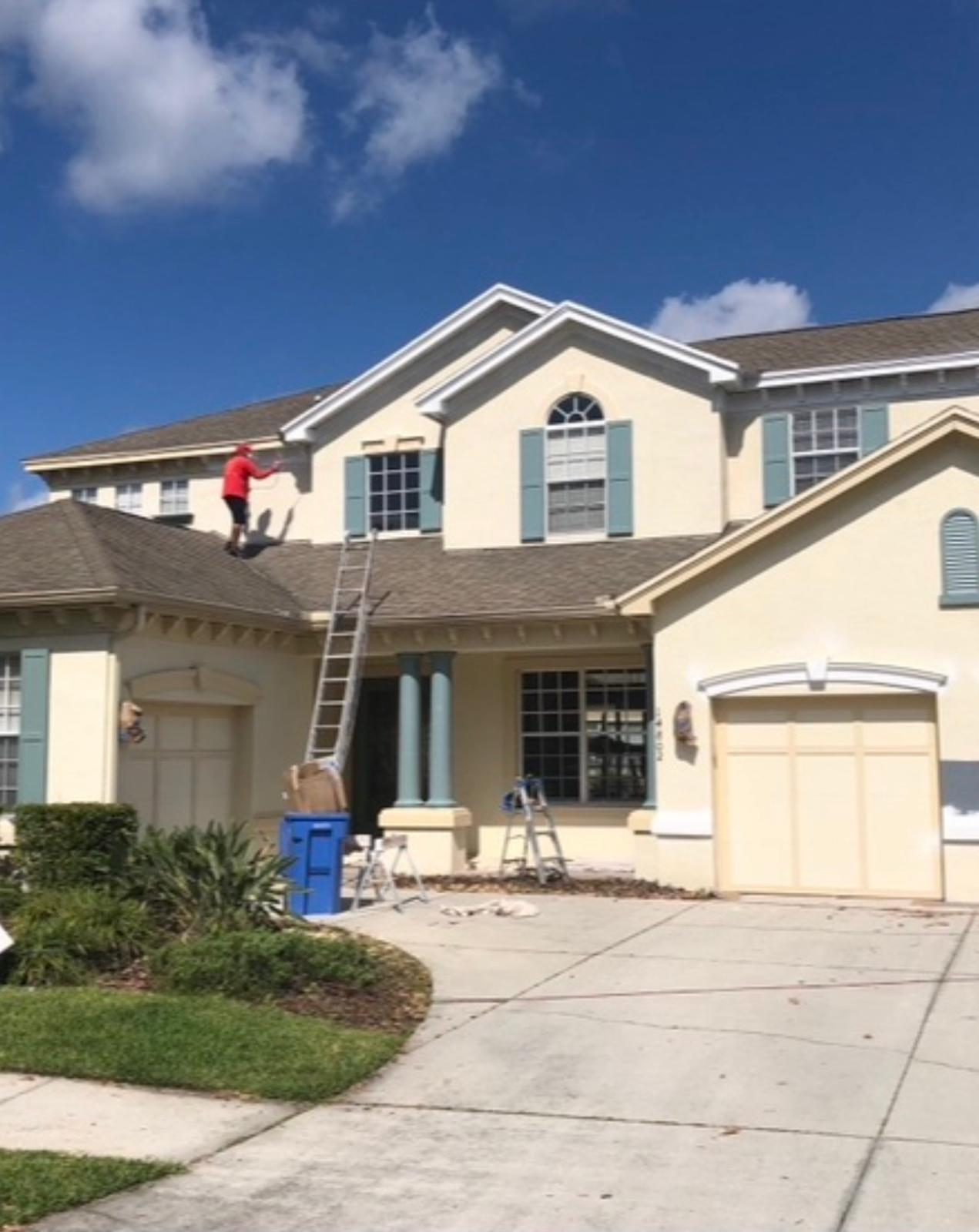Professional painter detailing two-story roofline trim, eaves, and exterior stucco on sunny afternoon in Odessa FL