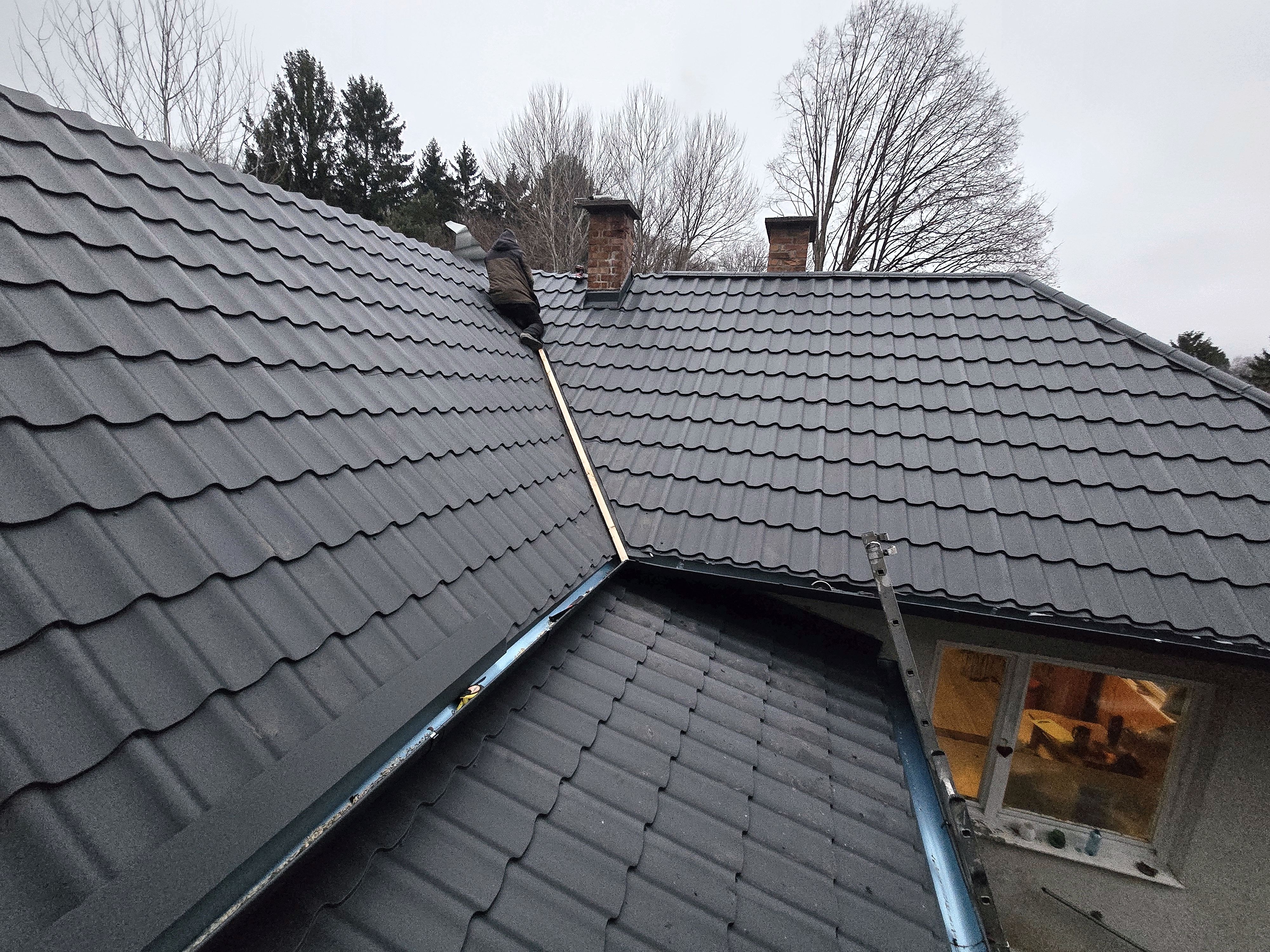 Eindeckung mit anthrazitfarbenen Metalldachpfannen an verwinkeltem Dach mit Vorbereitung der Spenglerkehle
