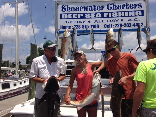 Anglers holding redfish and cobia at the Shearwater Charters sign in Biloxi