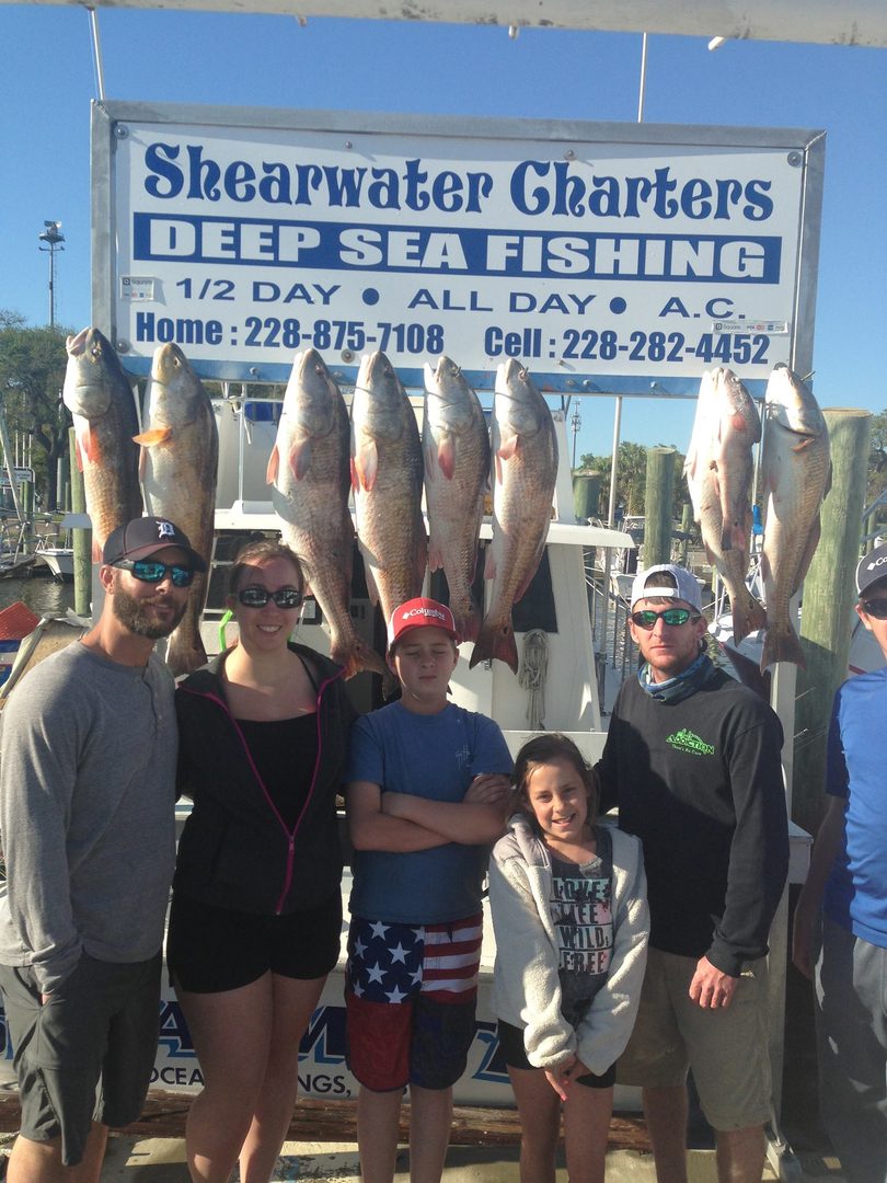 Family with kids in front of their redfish catch at the Shearwater Charters sign in Biloxi