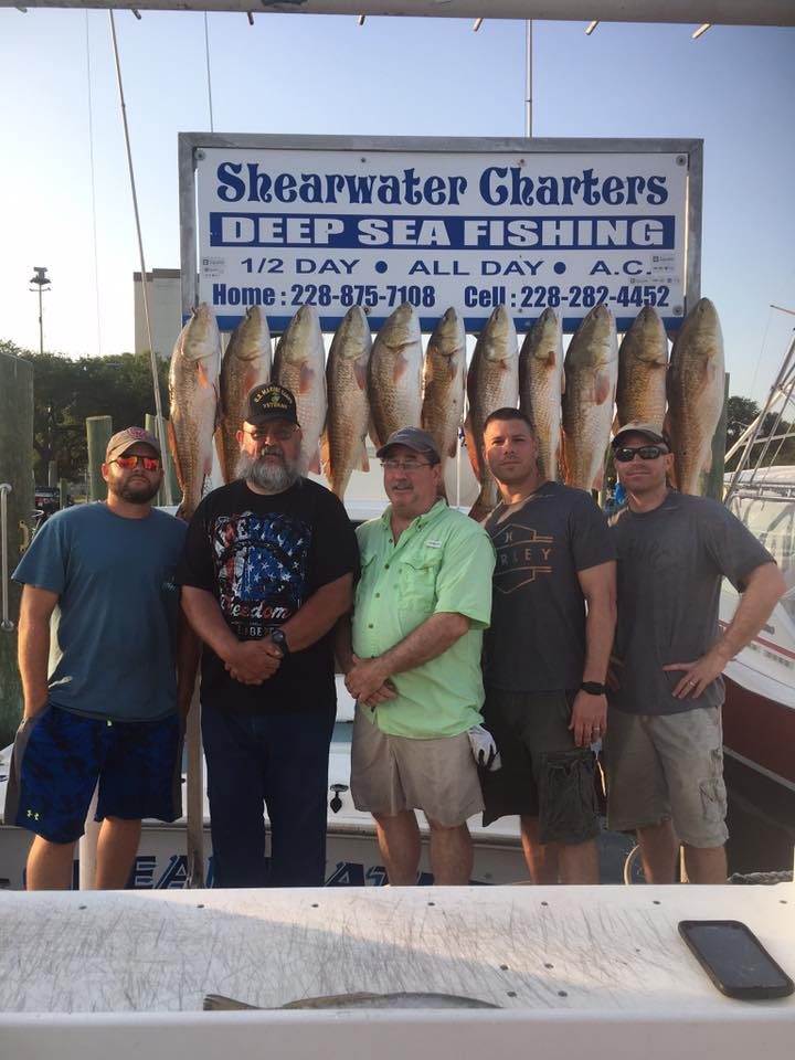 Group of five anglers with a limit of redfish at the Shearwater Charters sign in Biloxi