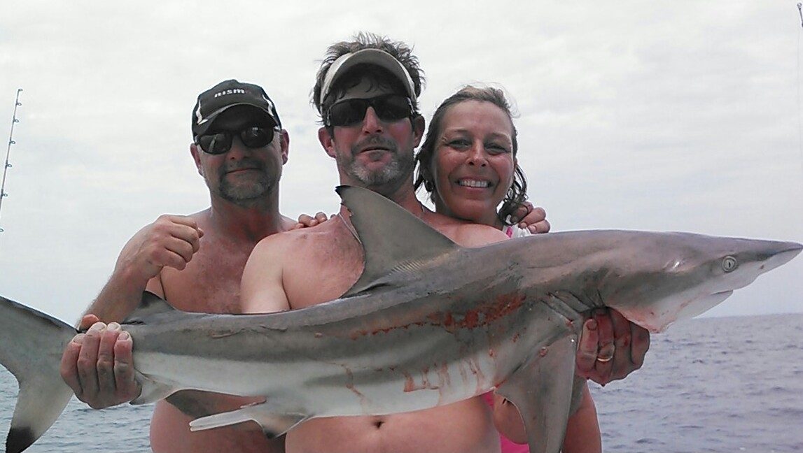 Three anglers holding a shark caught offshore on a 10-hour fishing trip from Biloxi