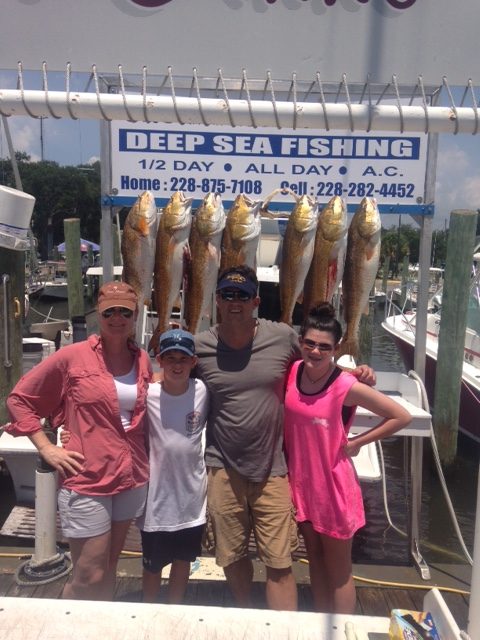 Family of four with redfish at the Shearwater Charters sign in Biloxi