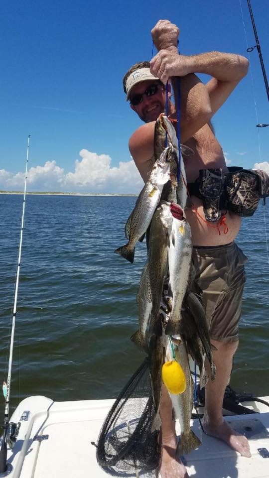 Angler holding a stringer of speckled trout near a Mississippi barrier island