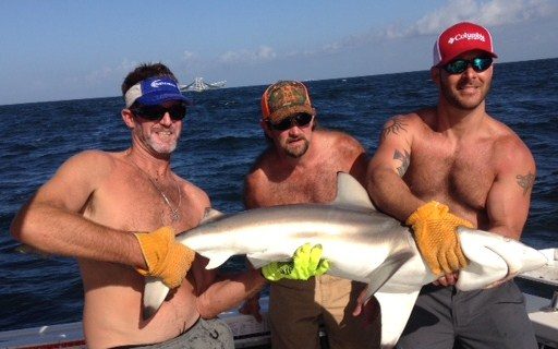 Three anglers holding a blacktip shark caught offshore on a 10-hour fishing charter from Biloxi