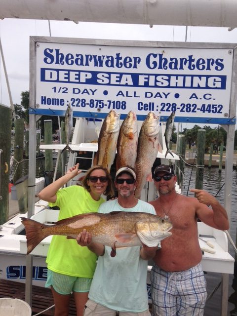 Three anglers celebrating a bull redfish at the Shearwater Charters sign in Biloxi