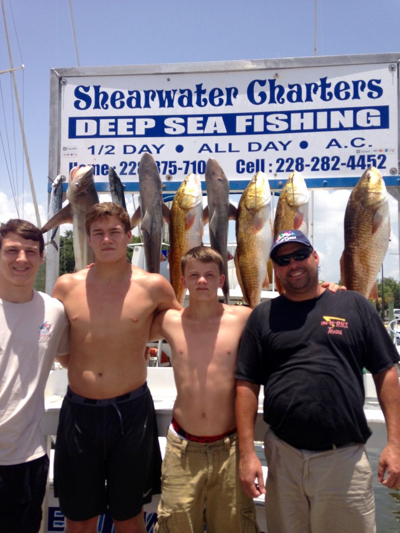 Father and sons with redfish and sharks at the Shearwater Charters sign in Biloxi