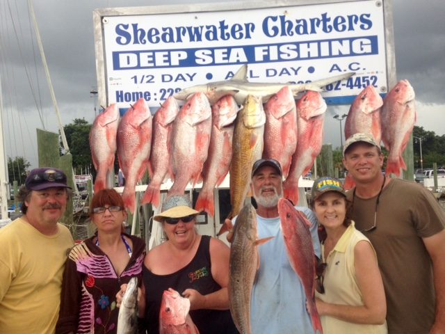 Group with red snapper, redfish and a shark at the Shearwater Charters sign in Biloxi