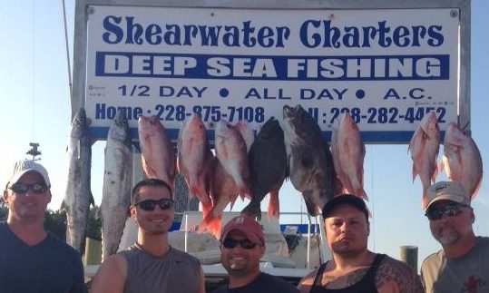 Group with red snapper and bottom fish hanging at the Shearwater Charters sign in Biloxi