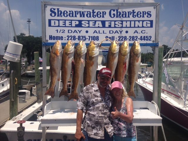 Couple in front of a limit of redfish at the Shearwater Charters sign in Biloxi