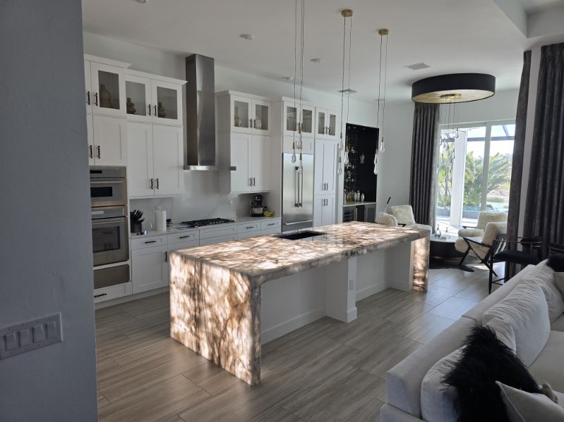Luxury custom kitchen island with luminous backlit translucent stone waterfall countertop and designer pendant fixtures