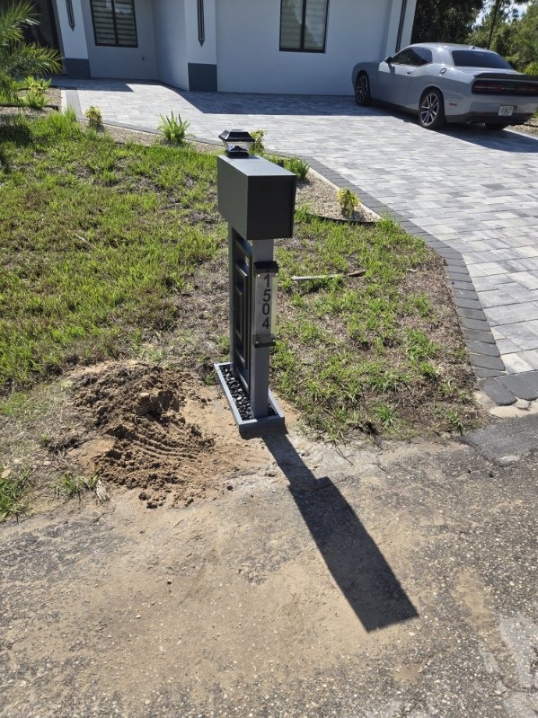 Modern architectural aluminum mailbox post with solar cap light, house numbers and decorative pebble base on driveway