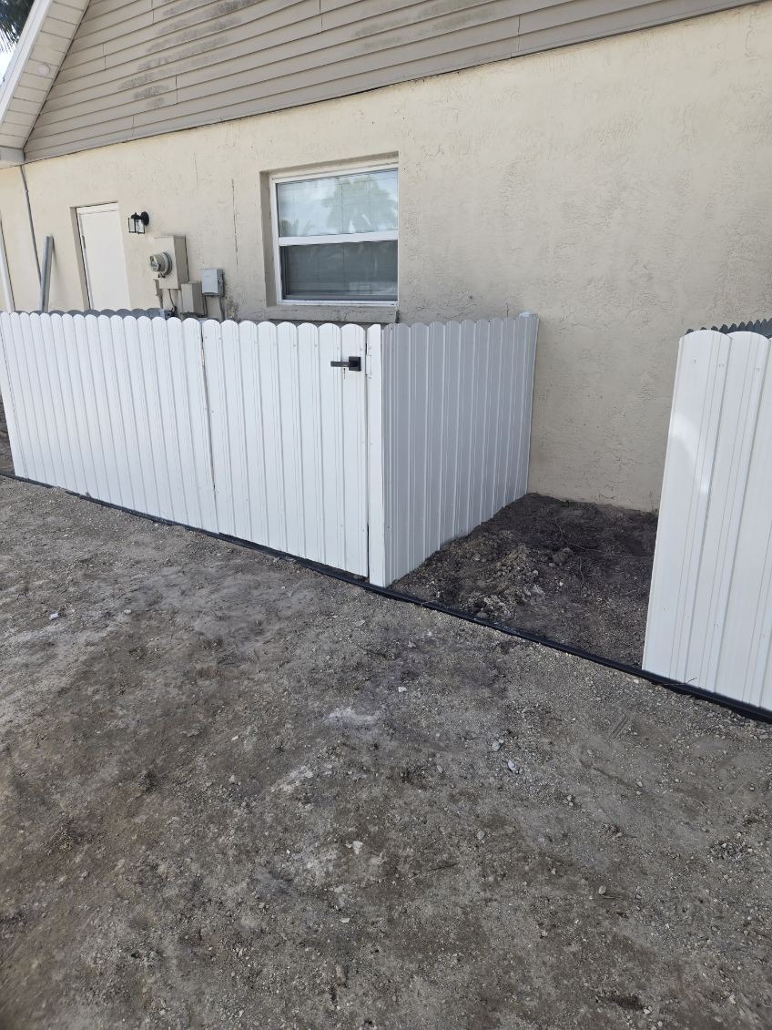 White scalloped vinyl privacy fence and gate enclosing residential home utility meters and AC equipment