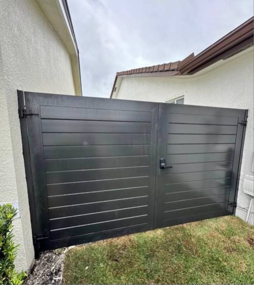 Modern matte black horizontal slat aluminum privacy double gate installed between Florida residential home walls