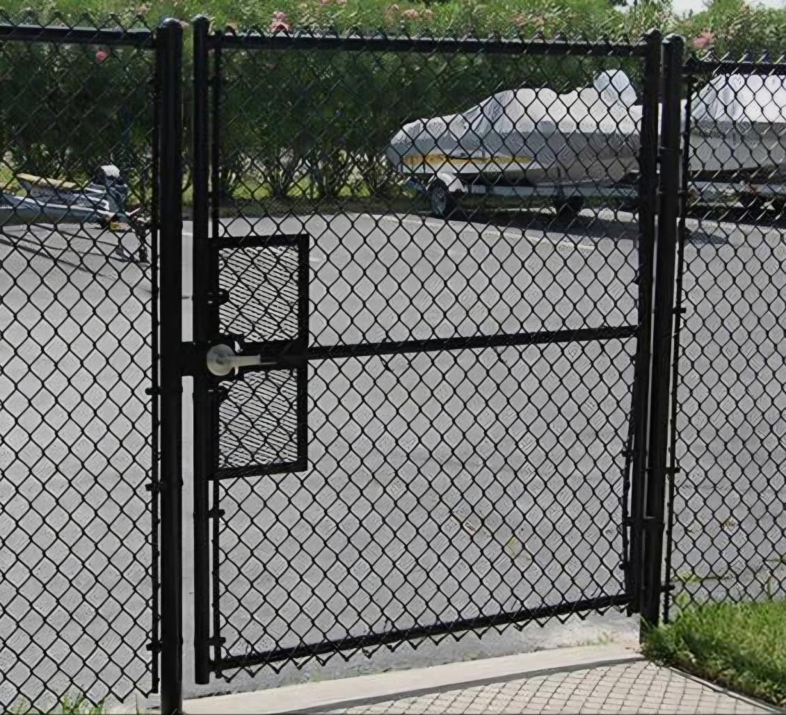 Black commercial chain link gate with heavy-duty metal mesh lock shield protecting parked boats and vehicles