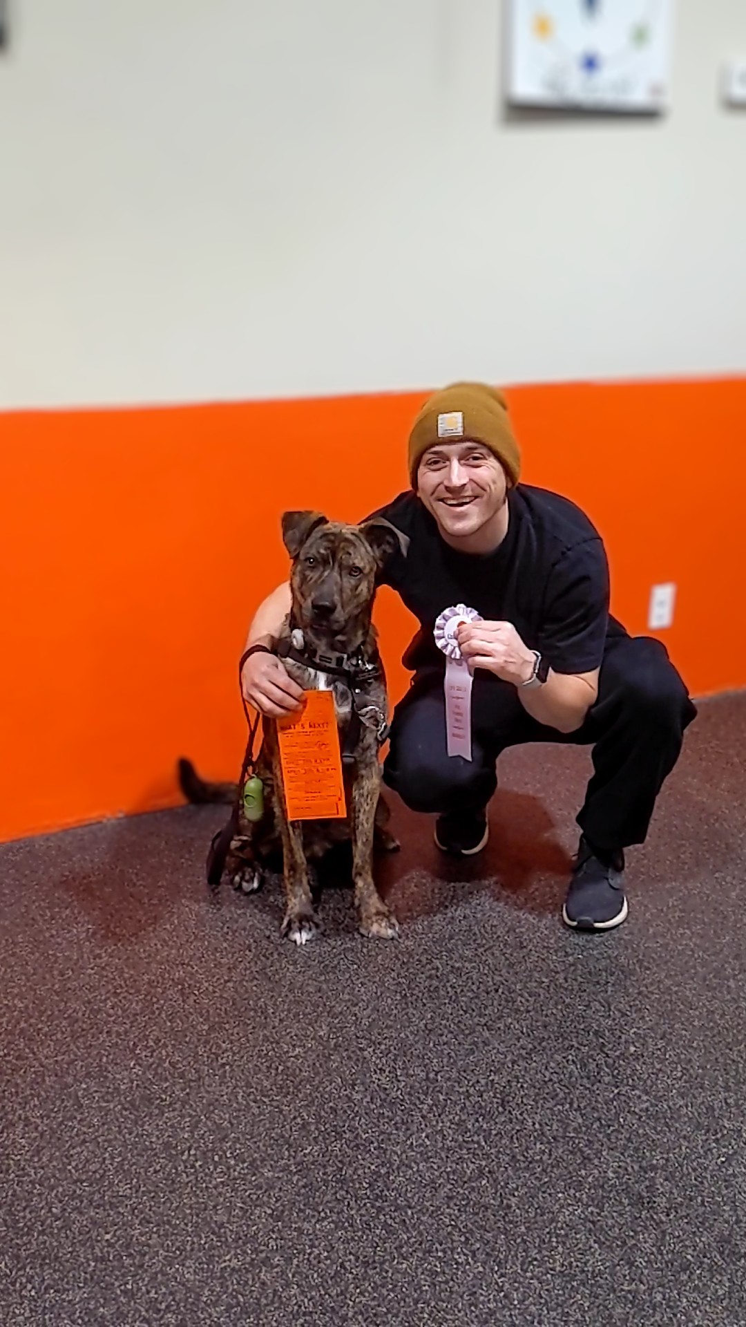 Life Skills graduate smiling with their brindle dog holding graduation ribbon and certificate