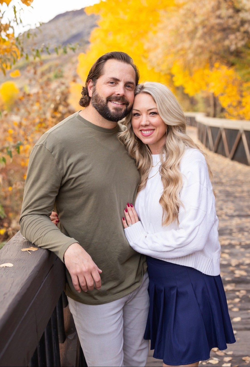 Kelli and Taylor together on a bridge surrounded by autumn leaves