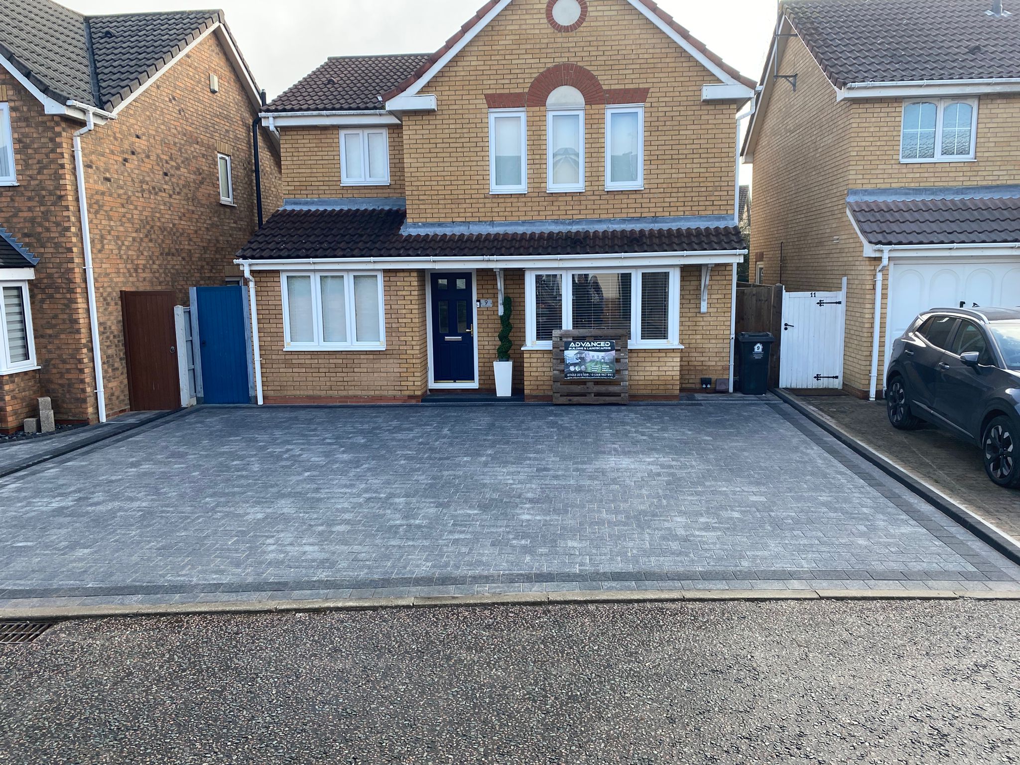 Full view of completed charcoal-bordered grey block paved driveway in front of brick house