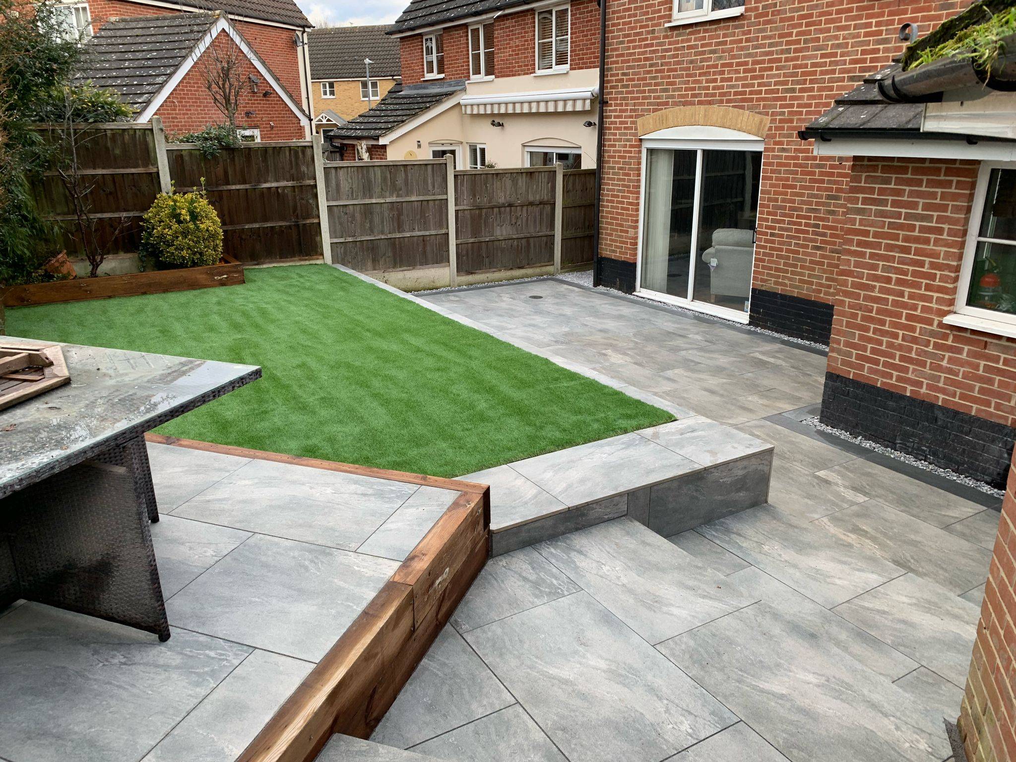 Split level garden with artificial grass lawn, porcelain patio, and raised timber planters in Essex