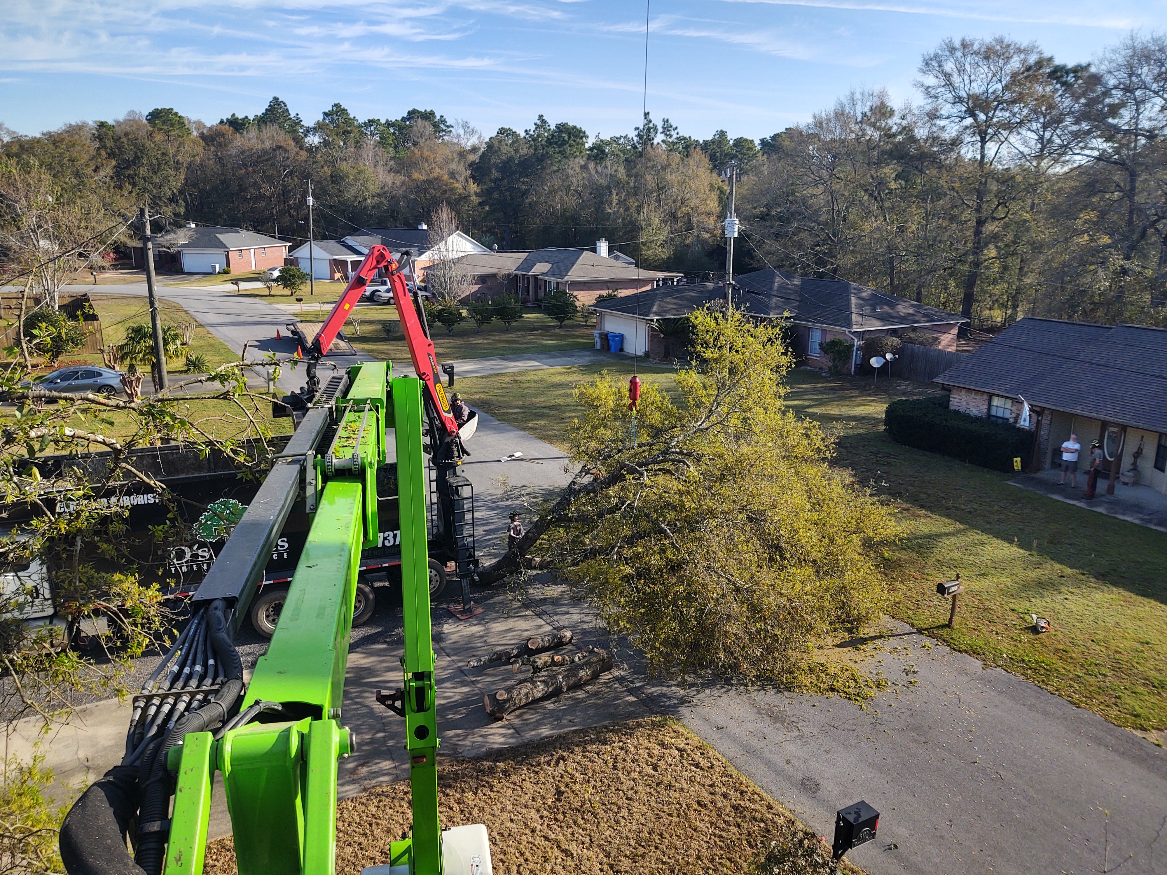 Aerial view of D's Trees crane removing massive storm-felled tree safely over a residential neighborhood