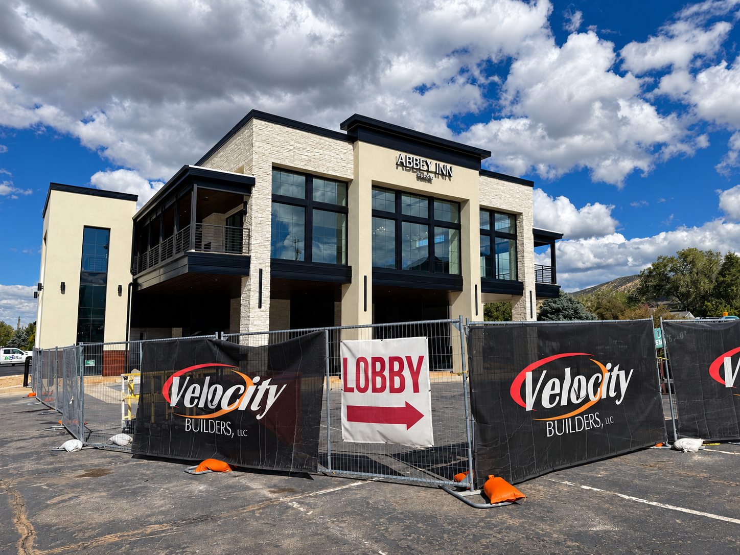 Abbey Inn new two-story lobby building exterior with natural stone veneer and Velocity Builders construction fencing