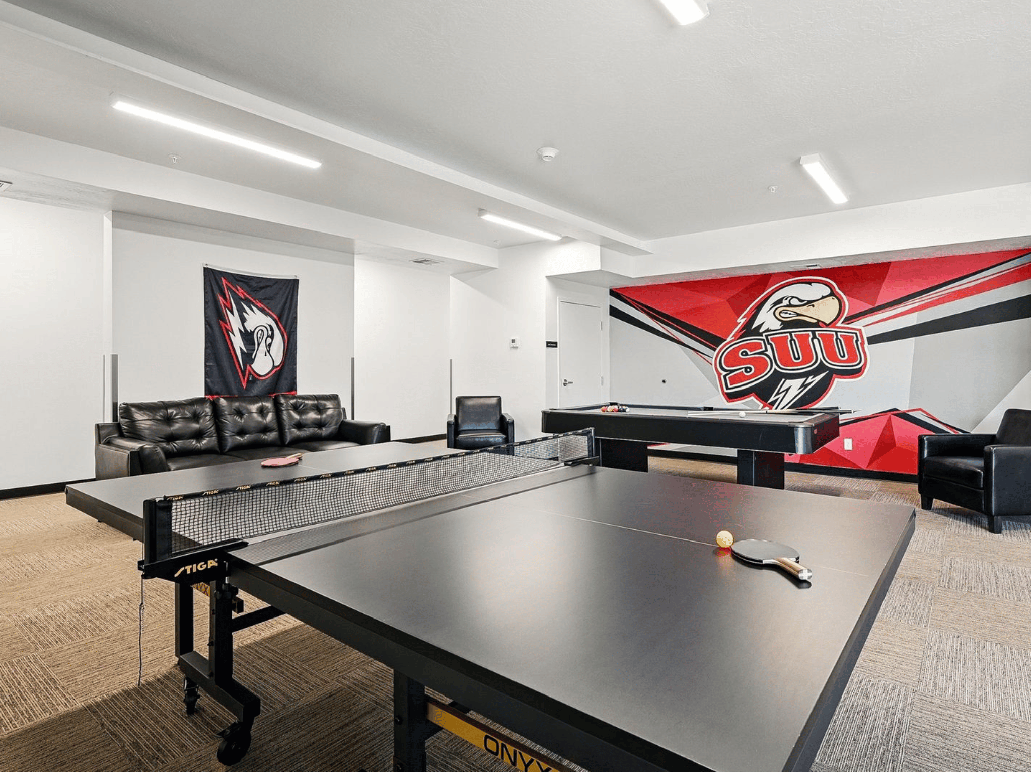 Student resident game lounge with ping pong table, billiards table, leather seating, and SUU graphics