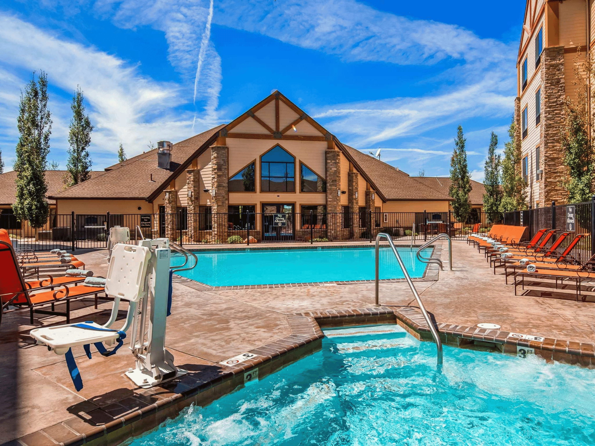 Outdoor swimming pool and hot tub spa terrace with chaise lounges and timber-framed hotel clubhouse