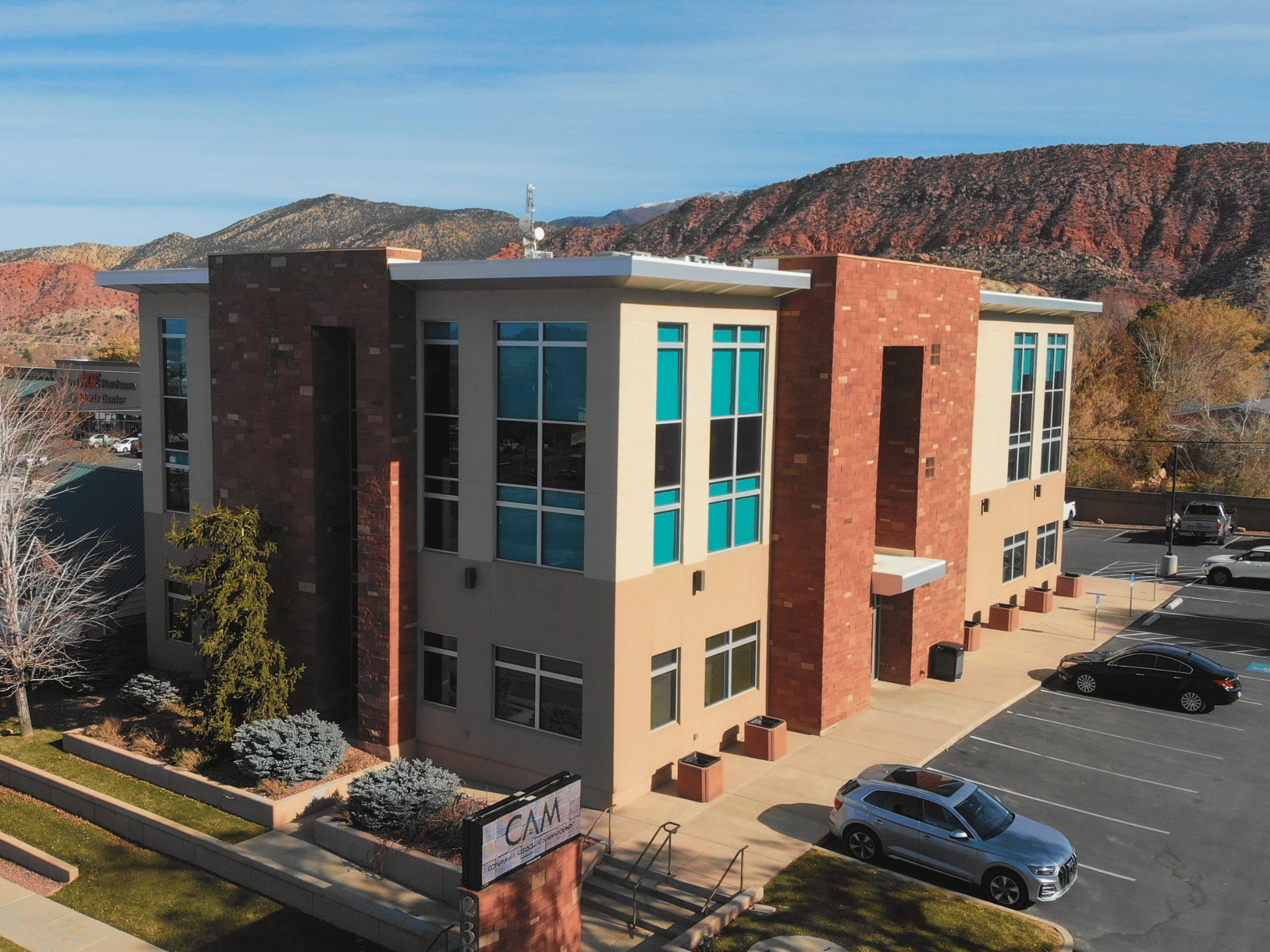 Two-story modern commercial office building with red brick and stucco facade, parking lot, and red rock mountains in Southern Utah