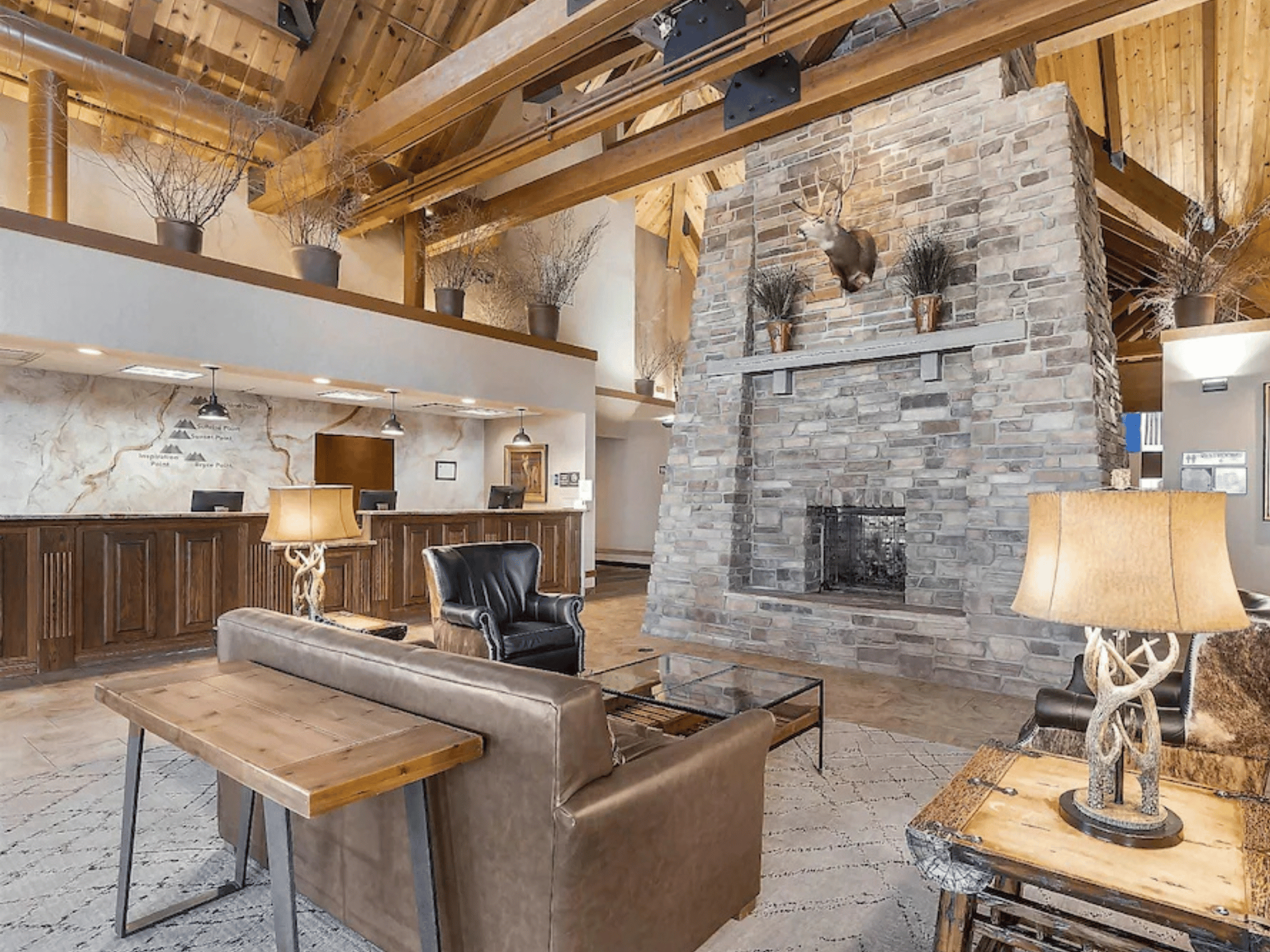 Grand lodge hotel lobby with floor-to-ceiling stone fireplace, timber truss ceiling beams, and reception desk