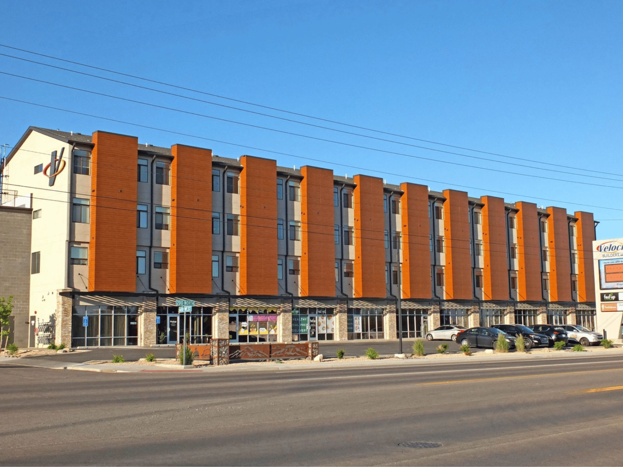 Modern four-story mixed-use multi-family building with warm wood-tone vertical architectural panels and ground-floor commercial storefronts at 200 North in Cedar City, Utah